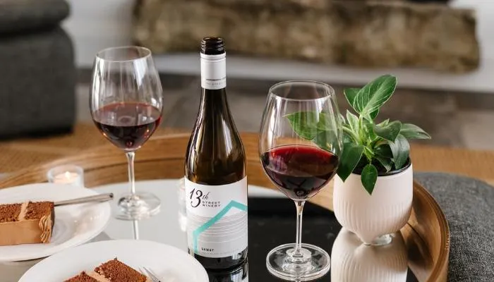 Two glasses of red wine are placed on a table with desserts. Between the glasses is a bottole from 13th Street Winery, one of Niagras top wineries