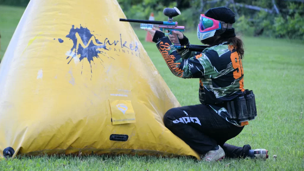 A Marked Adventure Paintballer kneels behind a yellow blind