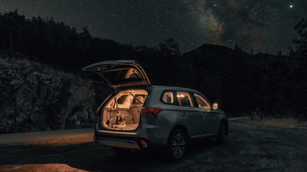 the Trunk of an SUV is open on a stary summer night. Inside the trunk is a pair of hiking boots