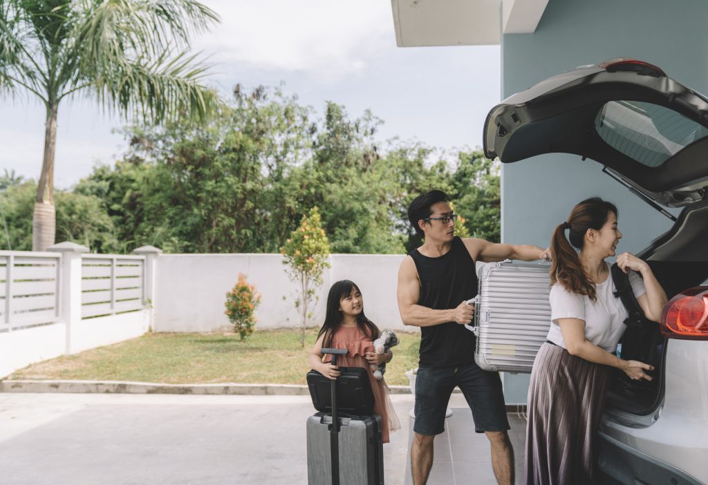 A family with one small young daughter loads up their car for a with suitcases for a summer adventure