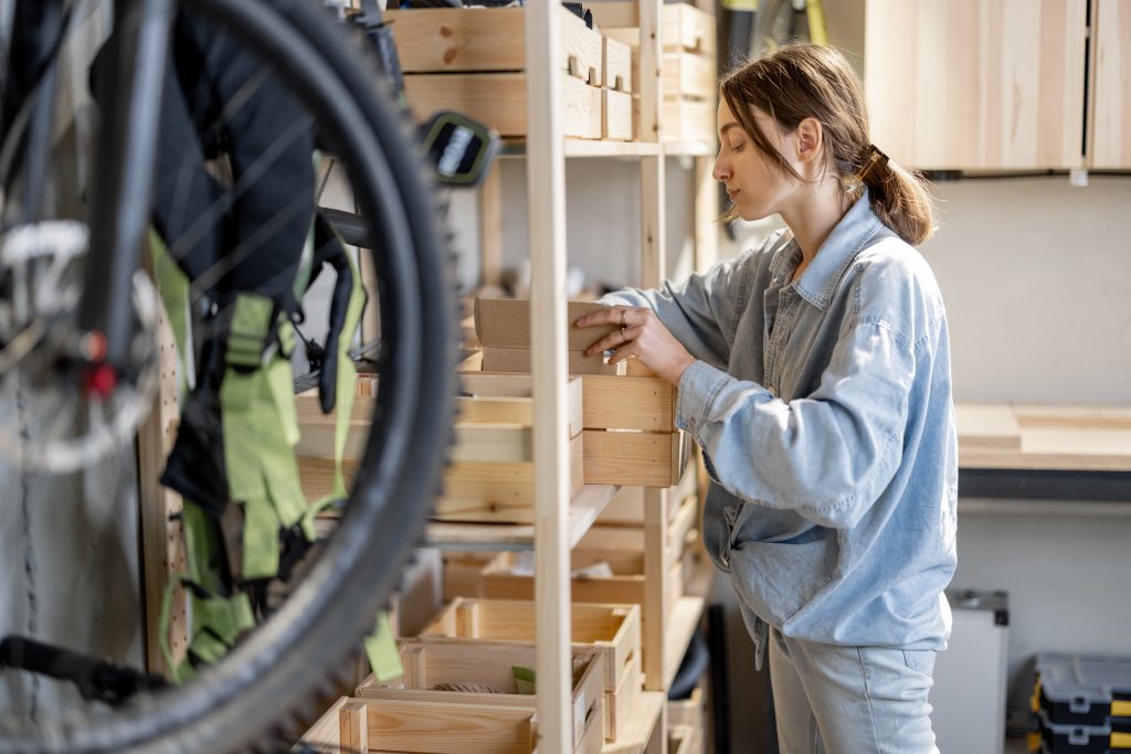 Young handywoman searching some working tools on a wooden shelves in the workshop. Concept of organization in home garage or storage