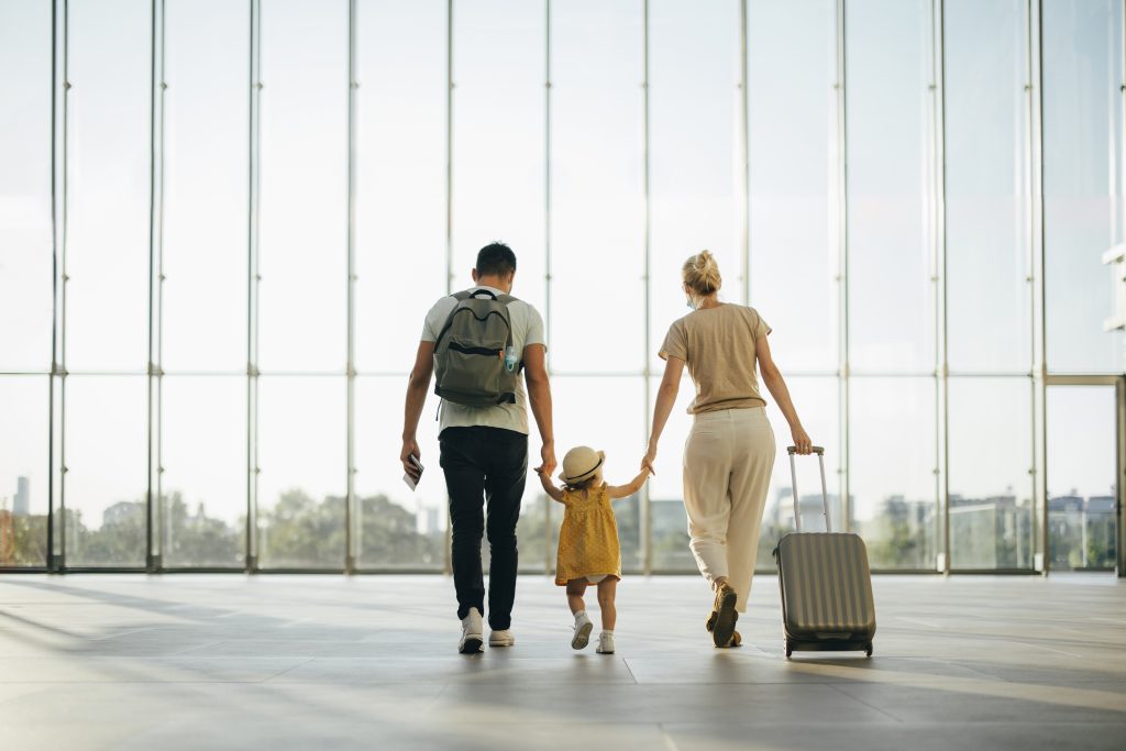 Back view of husband and his wife walking with their little girl and suitcase at the airport