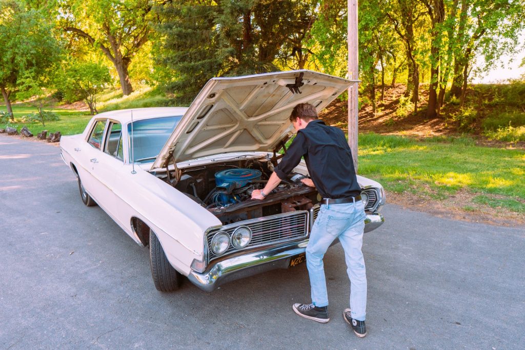 man standing in front of car, examines battery