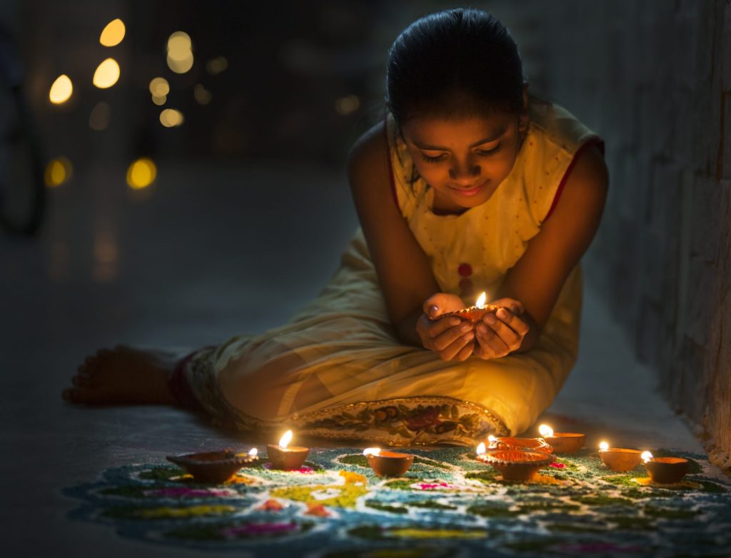 Girl making Rangoli and decorating with Oil lamps for Diwali