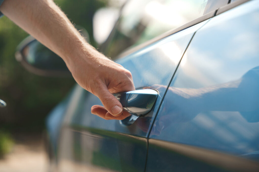 A close up of a man's hand, opening a car, holding a car door handle, we see it in a day light