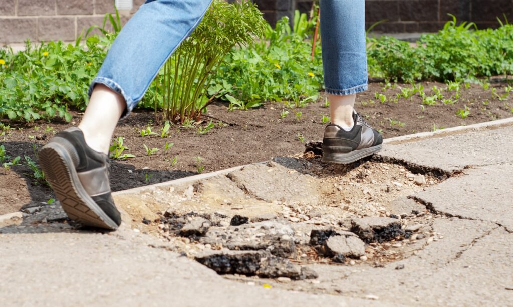 A person is walking past uneven cracks in the sidewalk