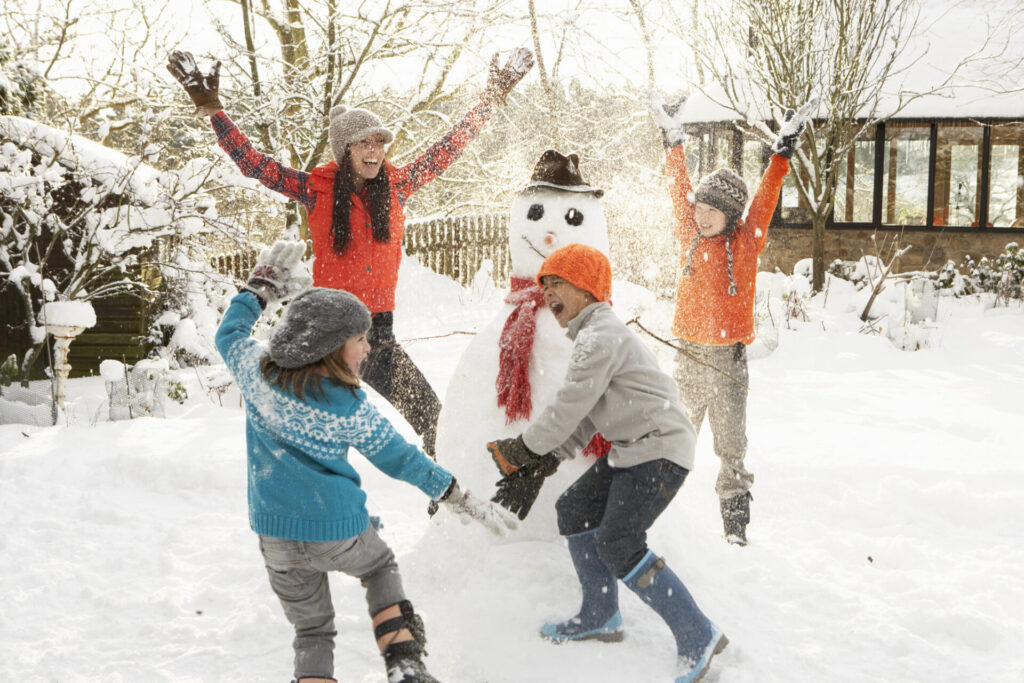 Happy mom and children building snowman in yard