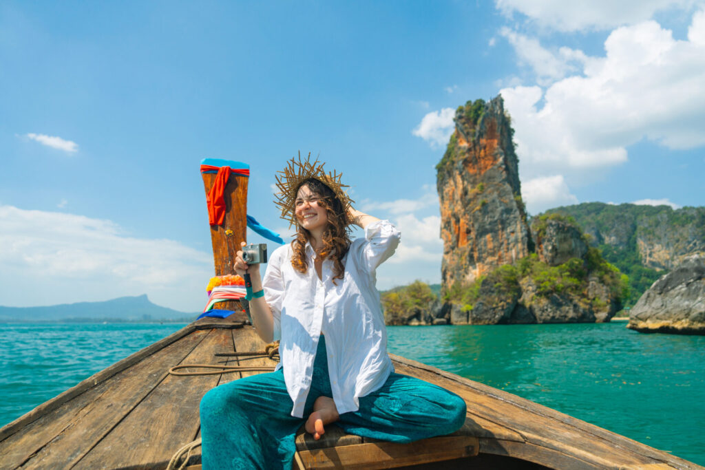 Cheerful woman traveling with Thai taxi boat and photographing with point and shoot camera