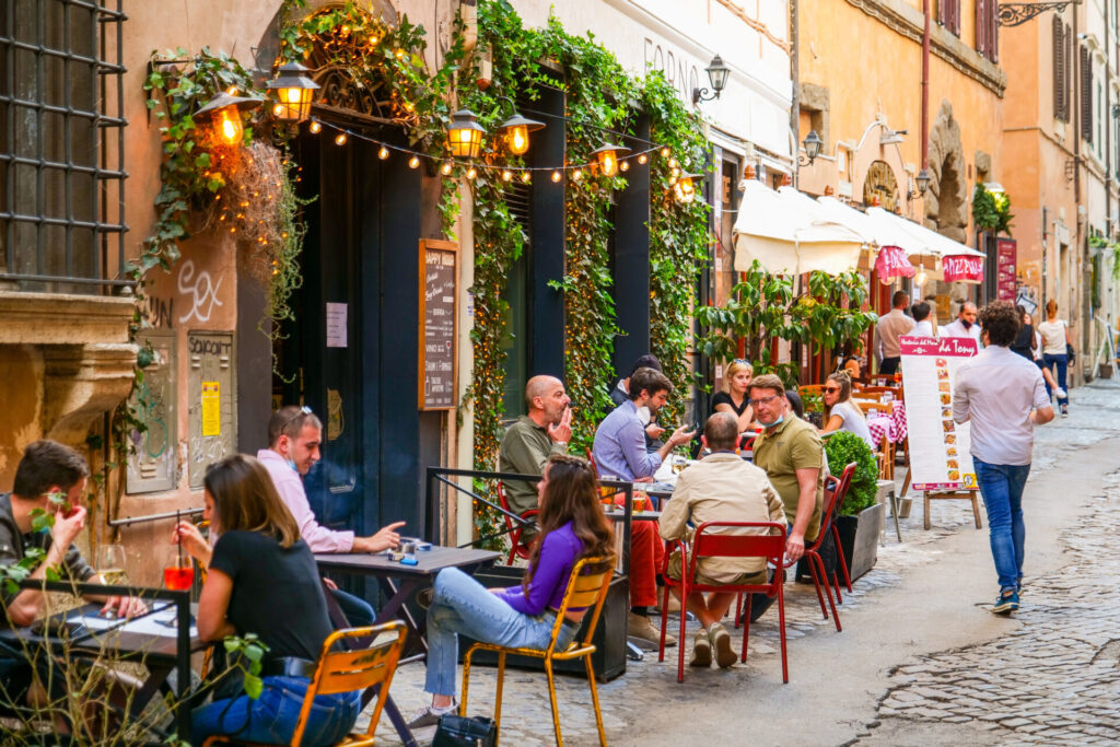 Some tourists enjoy an aperitif in a bistro along a stone alley in the Trastevere district in the heart of Rome