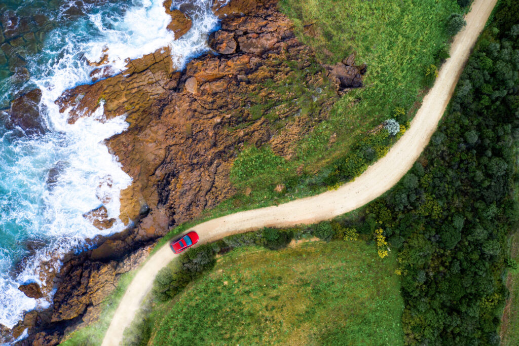 Driving on a seaside road approaching a beach, seen from above