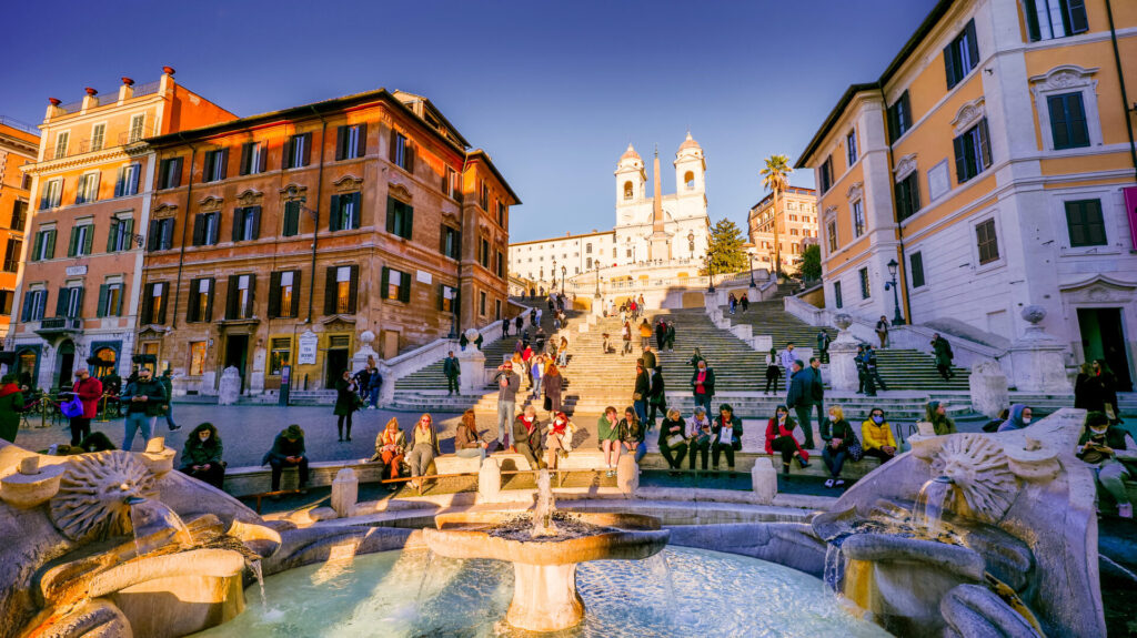 A warm sunset light illuminates the Barcaccia Fountain and Piazza di Spagna in the Baroque heart of Rome