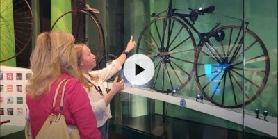 Two women in a museum looking at antique bikes