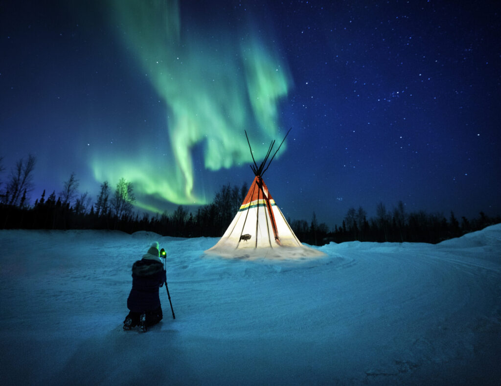 Aurora above lit teepee in Canada